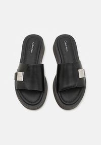 Sorte slidesandaler med en bred rem, lavet af glat materiale. Med et sølvmetallic accent og polstret fodseng for komfort.