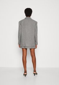 Musta-valkoinen ruudullinen ylipitkä bleiseri terävillä olkapäillä, pitkillä hihoilla ja kauluksella. Päällä lyhyen hameen kanssa.