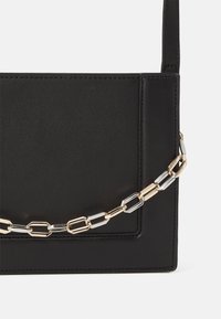 Zwarte neplederen handtas met een gladde textuur, voorzien van een gouden en zilveren kettingband, rechthoekige vorm en minimalistisch ontwerp.