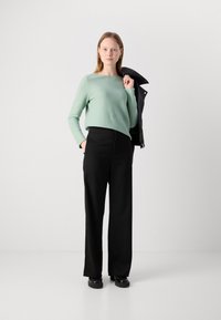 Mentazöld, hosszú ujjú felső, fekete, bő szárú nadrág és fekete bőrdzseki. Texturált anyag, laza szabás. Minimalista dizájn.