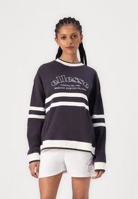 Sudadera de canalé azul marino oscuro con rayas blancas y logo, escote redondo, ajuste holgado. Combinada con pantalones cortos blancos que presentan un detalle de logo.
