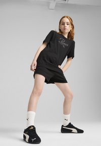 Camiseta negra con el logo de "Puma", combinada con pantalones cortos negros, calcetines blancos y zapatillas negras con detalles blancos. Vestimenta atlética simple y casual.