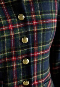 Woolen plaid fabric featuring dark blue, green, and red patterns, enhanced by gold buttons with emblems, showcasing a tailored design.