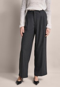 Weite, dunkelgraue Hose mit Falten, aus strukturiertem Stoff. Kombiniert mit einem leichten Strickpullover und schwarzen spitzen Ballerinas.