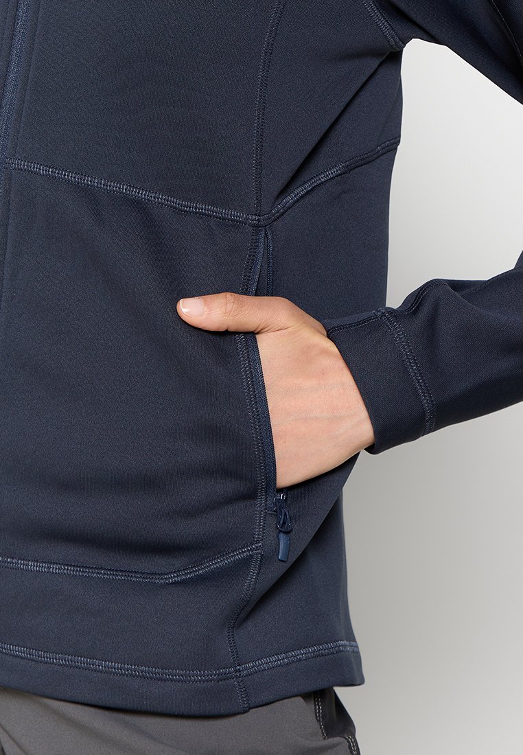 Chaqueta de rendimiento en navy hecha de material elástico, con un bolsillo con cremallera y costuras planas para mayor comodidad. Detalle destacado en la parte del brazo.