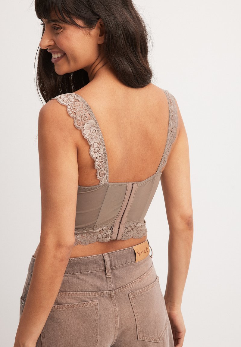 Mauve blondelace bralette med brede, mønstrede stropper, en kroklukning bagpå og en blomstret blondelace-kant langs bundkanten.
