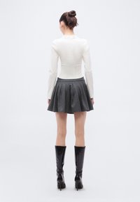 Bijeli uski top s dugim rukavima, siva plisirana mini suknja s tankim prugama i crne čizme do koljena s petom, prikazani s leđa.