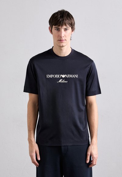 Kurzarm-Navy-T-Shirt aus Baumwolle mit einem zentralen weißen Logo, das in einer lässigen Schriftart "EMPORIO ARMANI Milano" liest.