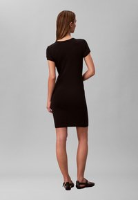 Czarna sukienka z krótkim rękawem o dopasowanym kroju, z krawędzią sięgającą kolan, bezszwowym tyłem i prostym okrągłym dekoltem, zestawiona z czarnymi butami.
