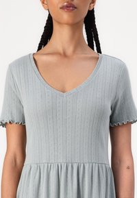 Vestido azul-claro de mangas curtas com decote em V, listras verticais texturizadas e acabamentos das mangas com babados. O tecido parece suave e leve.