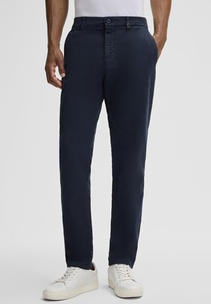 Marineblaues Slim-Fit-Hosen aus leichtem Stoff, mit Reißverschluss, Knopfverschluss und zwei seitlichen Taschen. Kombiniert mit weißen Sneakers.