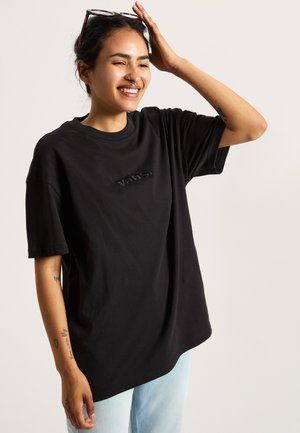 Zwart katoenen t-shirt met een ontspannen pasvorm, voorzien van een geborduurd "vans." logo op de borst, gedragen met lichtblauwe jeans.