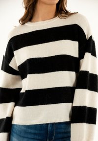 Maglione a righe bianco e nero, realizzato in un tessuto morbido, presenta un collo girocollo e una vestibilità comoda, abbinato a jeans di denim.