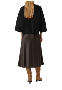 Czarny prążkowany sweter z szerokimi rękawami, zestawiony z długą, gładką brązową spódnicą oraz brązowymi zamszowymi kozakami za kolano na niskim obcasie.