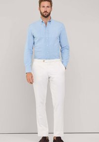 Camisa de botones a rayas de color azul claro combinada con pantalones blancos. El conjunto tiene un corte ajustado, con un sutil detalle de hardware en los pantalones.