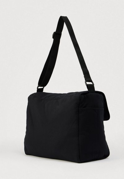 Μαύρο τσαντάκι ταχυδρόμου με μαλακό σχεδιασμό, ρυθμιζόμενο ιμάντα ώμου και λείο υφασμάτινο υλικό. Ο πλαϊνός θύλακας είναι ορατός.