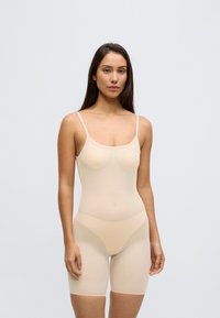 Lekki body w kolorze nude, bezszwowy, z cienkimi ramiączkami i dopasowanym krojem, o gładkiej fakturze i długości do połowy uda.