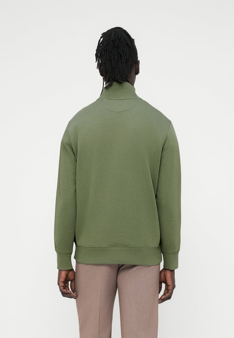 Sudadera verde con cuello alto, hecha de tela suave. Presenta puños y dobladillo acanalados, con una textura lisa. Vista trasera.