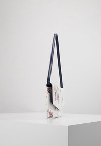 Blomstermønstret taske i hvid kunstlæder med en marineblå strop og klaplukning. Slim rektangulær form, glat tekstur.