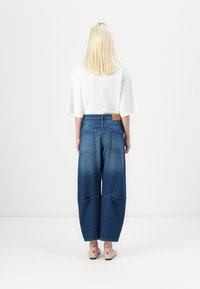 Wide-leg blue denim jeans with a faded wash, featuring two back pockets. Paired with a white top and light pink shoes.