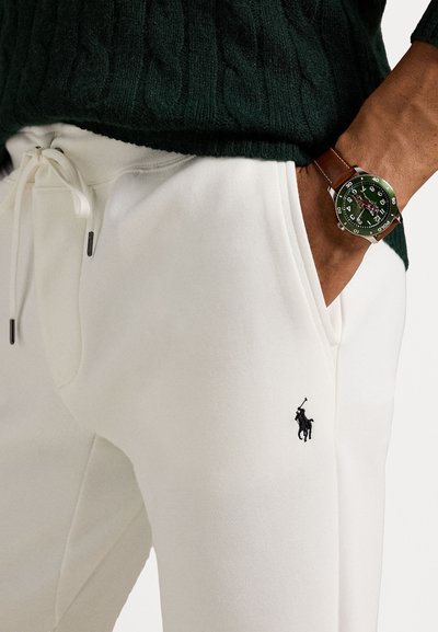 Bijele pamučne jogger hlače s vezicom, s malim crnim polo logom. Model nosi zeleni džemper od pletene vune i zeleni sat.