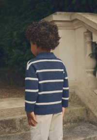 Maglione a righe blu navy con strisce bianche, trama lavorata a maglia e colletto polo, abbinato a pantaloni cargo beige chiaro.