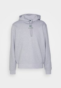 Sweat à capuche gris clair avec cordons sur le devant et petit logo vert Lacoste centré au-dessus du texte sur la poitrine.