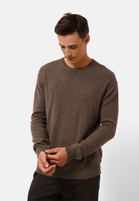 Brauner, gestrickter Pullover mit Rundhalsausschnitt, gerippten Bündchen und Saum. Weiche Textur mit lässiger Passform, über dunklen Hosen getragen.