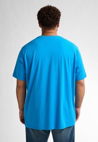 Tricou din bumbac albastru, cu mâneci scurte și guler rotund, având o croială lejeră. Vederea din spate arată o textură netedă și un design simplu.