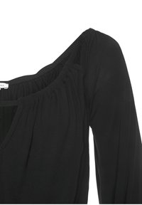 Černý top s dlouhými rukávy, s výstřihem do V, nařaseným výstřihem a měkkou tkaninou s hladkým povrchem. Viditelný detail švu na rameni.