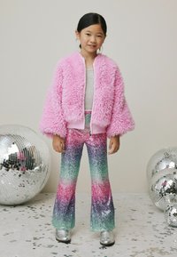 Pink fuzzy bomber jacket, gray top, and multicolored sequin bell-bottom pants. Silver shoes complement the vibrant outfit.