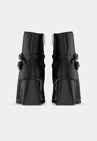 Mustad mustad ankle boots sujuva nahkviimistlusega, millel on kaks kullatooni klambrit ja lukud taga, ning jäme konts.