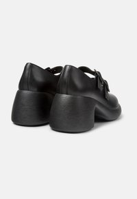 Scarpe in pelle nera con punta arrotondata, tacco bloccato testurizzato e dettaglio a fiocco decorativo. Finitura liscia, cinturino alla caviglia regolabile.