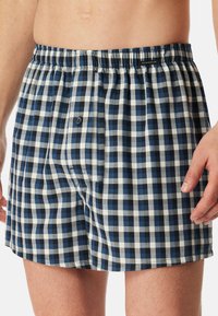 Boxers à carreaux bleus et blancs avec une taille élastique et une fermeture à bouton unique à l'avant, fabriqués en tissu respirant.