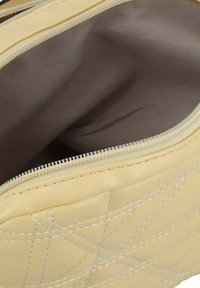 Mochila de cuero amarilla con diseño acolchado y costuras blancas. Interior forrado con tela suave marrón y asegurada con un cierre de cremallera.