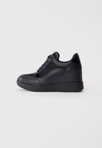 Sneaker nera con tomaia in rete testurizzata, dettagli in pelle lucida e suola a cuneo. Presenta lacci e un dettaglio laterale con marchio.