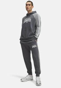 Grå hættetrøje med hvid "Under Armour" tekst, med grå accenter. Sammen med matchende sweatpants, der også har det samme brand.