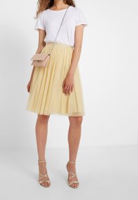 Una gonna in tulle gialla con un design a pieghe è abbinata a una T-shirt bianca aderente. Una piccola borsa rosa pende da una tracolla in catena argentata.