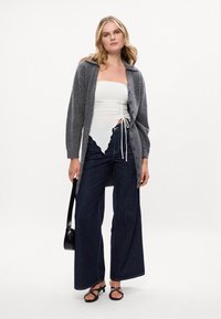 Γκρι πλεκτή ζακέτα με γιακά, σε συνδυασμό με λευκό τοπ με ραφές και φαρδιά τζιν σκούρου χρώματος. Μαύρα σανδάλια και μικρή μαύρη τσάντα.