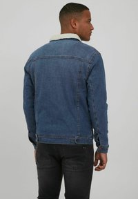 Chaqueta de denim en azul oscuro con un collar de sherpa blanco, que presenta un diseño estructurado, puños abotonados y detalles de costura en la parte posterior.