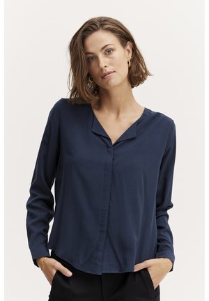 Blusa a maniche lunghe blu navy con scollatura a V, texture liscia, chiusura frontale con bottoni e orlo leggermente curvo.