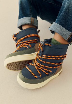 Scarpe alte in materiali blu navy e verde oliva, con lacci arancioni a fantasia e una suola in gomma testurizzata. Presentano un supporto per la caviglia imbottito.