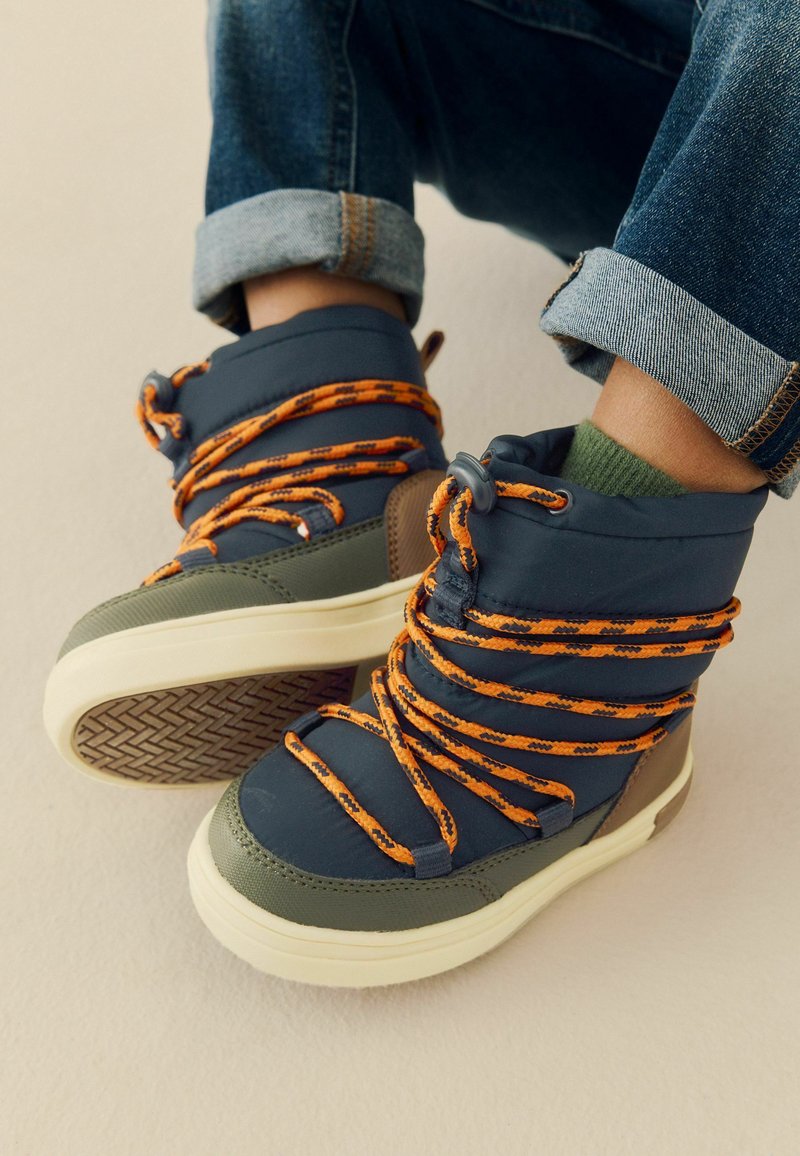 Höga skor i marinblå och olivgröna material, med mönstrade snören i orange och en texturerad gummisula. Har vadderat stöd runt ankeln.