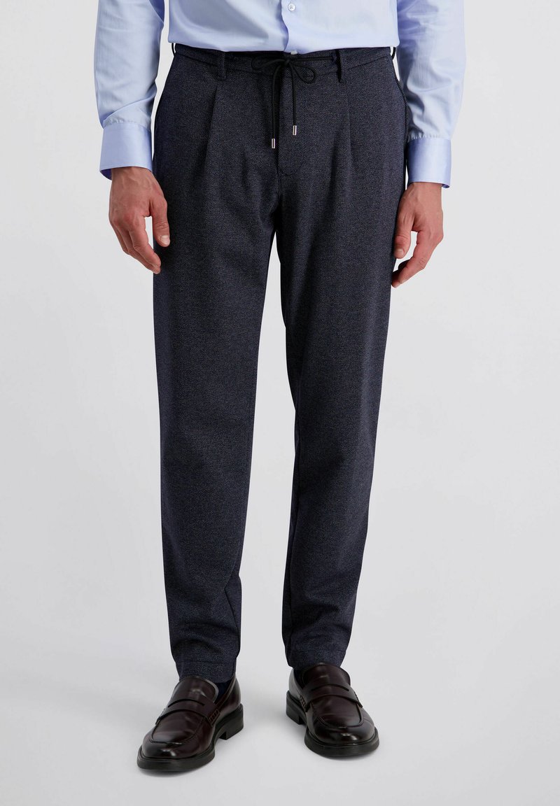 Marineblauwe geprinte broek met een drawstring taille, plooien aan de voorkant en taps toelopende benen, gecombineerd met bruine instappers.