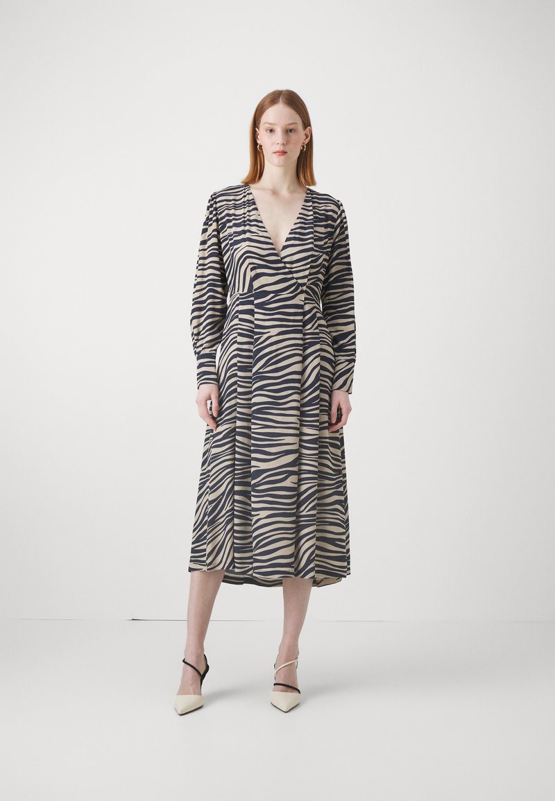 Pitkähihainen, vyötärölle sidottu mekko zebra-raidoilla, jossa on kermaista, laivastonsinistä ja vaaleaa väriä. Mekossa on runsaat hihat ja syvä V-pääkallo.