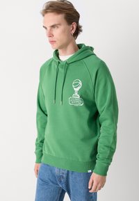 Πράσινη φούτερ μπλούζα από βαμβάκι με μπροστινή γραφική απεικόνιση ενός τροπαίου μπάσκετ. Διαθέτει τσέπη καγκουρό και ριμπ ύφανση στους μανικιών και στο τελείωμα.