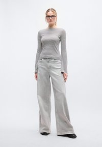 Ριγέ μακρυμάνικη μπλούζα σε μαύρο και άσπρο, συνδυασμένη με φαρδιά γκρι τζιν παντελόνια. Λείες υφές και άνετη εφαρμογή. Μαύρα παπούτσια ολοκληρώνουν την εμφάνιση.