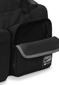 Svart nylon sports duffel bag med glidelås hovedrom, frontlomme med grå kant og et Nike-logo-patch på siden.