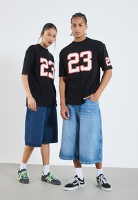 Svarta oversized T-shirtar med djärva röda "23"-grafik, i kombination med denim culotter. Skorna inkluderar sneakers med kontrasterande snören.
