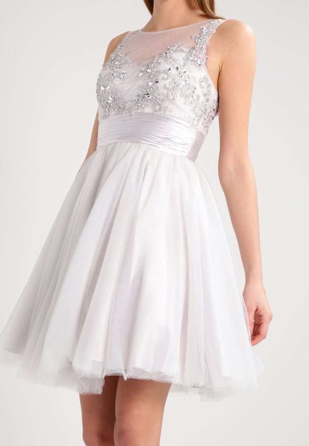 Robe de cocktail blanche sans manches avec corsage transparent orné, ceinture en satin et jupe en tulle pleine se terminant au-dessus des genoux.